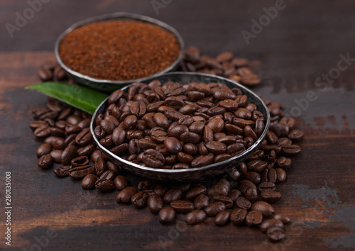 Fresh raw organic coffee beans with ground powder and coffee tree leaf on wooden background.