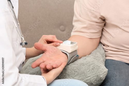 Nurse measuring blood pressure of elderly man against grey background  closeup. Assisting senior generation