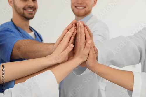 Team of medical workers holding hands together on light background, closeup. Unity concept
