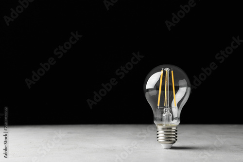 Vintage lamp bulb on light table against black background. Space for text