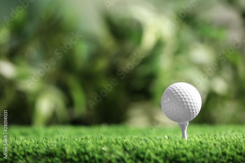Golf ball with tee on artificial grass against blurred background, space for text