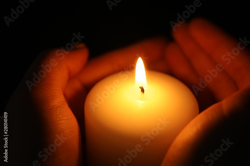 Woman holding burning candle in darkness, closeup