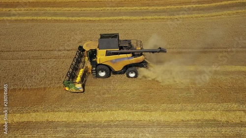 Side view of the harvester red and blue tractor, producing cleaning yellow rapeseed at farmers ' fields. The raw material is poured from the agricultural machine into a brown trailer, the heat comes