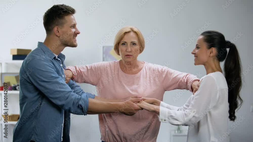 Mother-in-law pushing young man and woman holding hands, interference in family Mother-in-law pushing young man and woman holding hands, interference in family