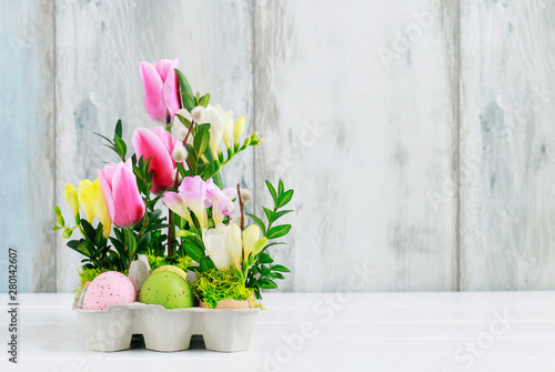 Easter floral decoration with colorful eggs, tulips, freesias and buxus.