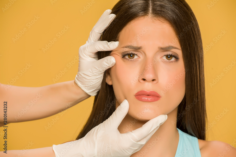 Doctor's hands checking the wrincles of a young woman on yellow background Doctor's hands checking the wrincles of a young woman on yellow background