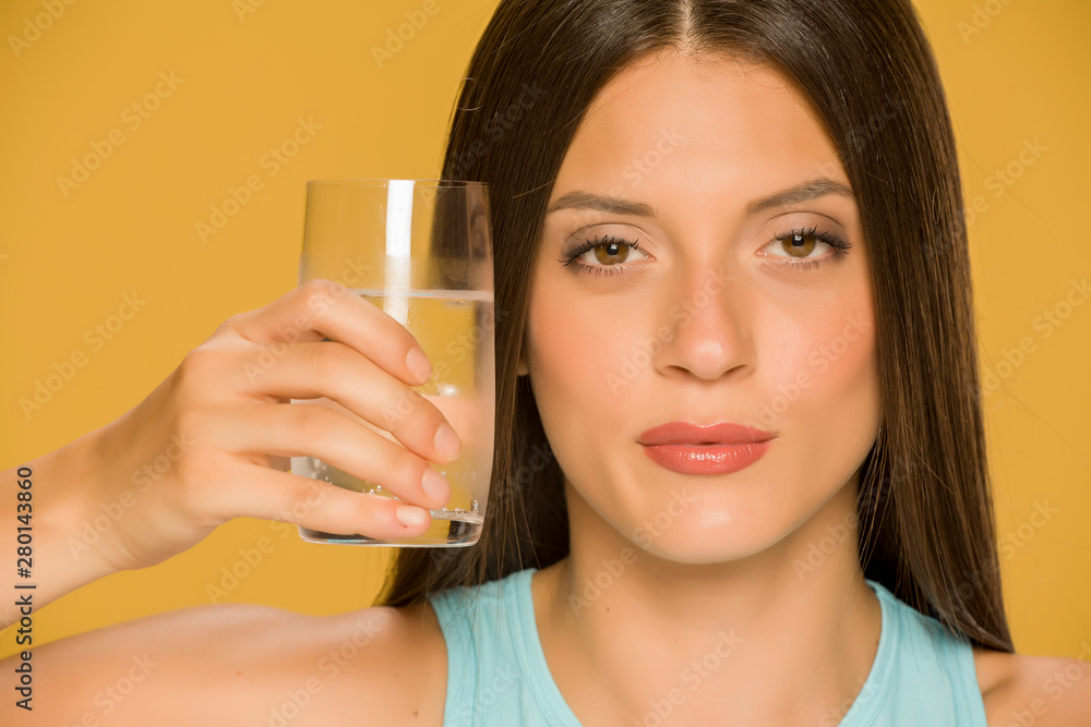 Young woman holding glass of water on yellow background Young woman holding glass of water on yellow background