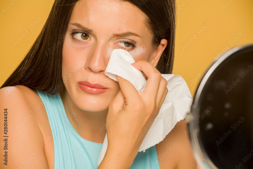 Young woman cleaning her face with wet wipes on yellow background Young woman cleaning her face with wet wipes on yellow background
