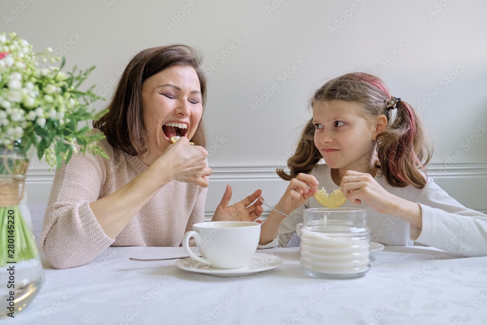 Laughing mother and daughter drinking from cups and eating lemon. Laughing mother and daughter drinking from cups and eating lemon.