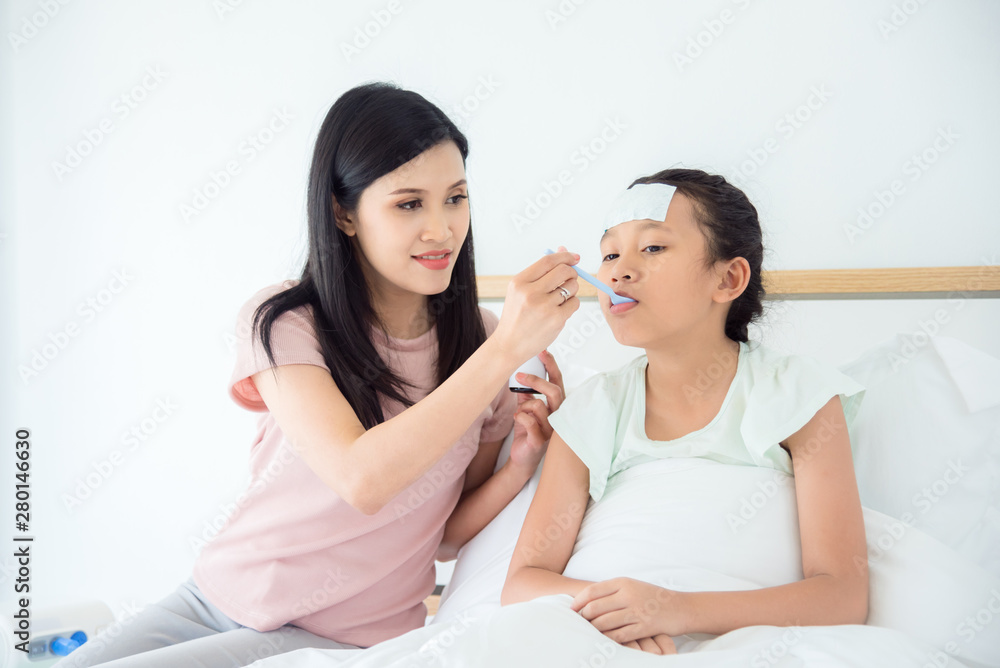 Young asian girl taking syrup medicine from her mother while sitting on bed in bedroom Young asian girl taking syrup medicine from her mother while sitting on bed in bedroom