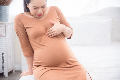 Photography Asian pregnant woman sitting on bed suffing from heart burn in third trimester
