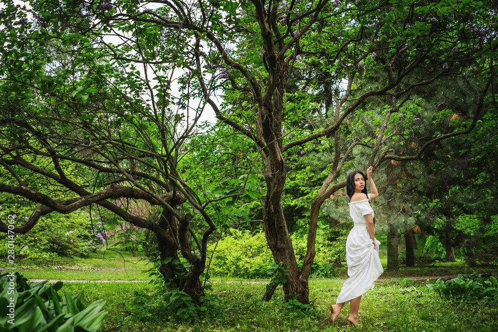 Beautiful young woman wearing elegant white dress walking on a forest path Beautiful young woman wearing elegant white dress walking on a forest path