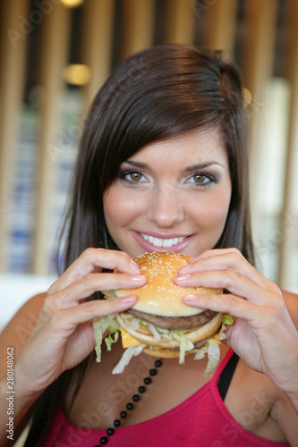 Jolie jeune femme brune mangeant un Hamburger dans un fast food