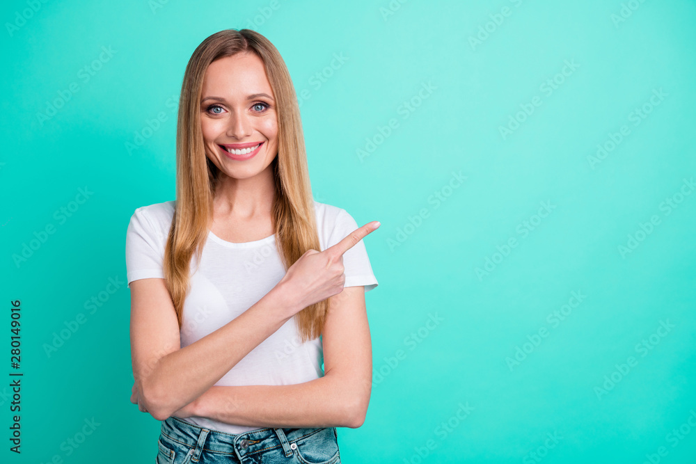 Portrait of lovely woman showing her finger indicating ads wearing denim jeans isolated over teal turquoise background Portrait of lovely woman showing her finger indicating ads wearing denim jeans isolated over teal turquoise background