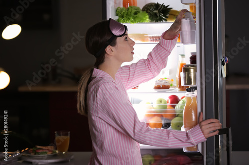 Obraz na plátne Beautiful young woman choosing food in refrigerator at night
