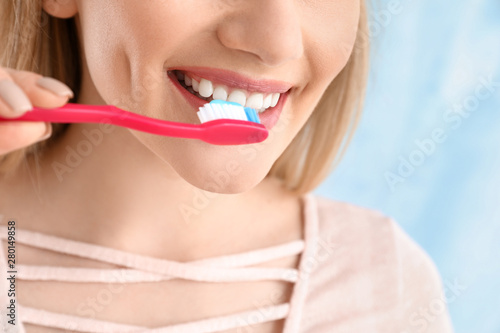 Beautiful woman cleaning teeth on light background  closeup