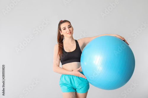 Young sporty woman with fitball on grey background