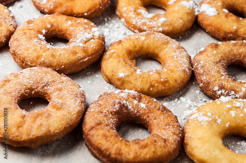 Many homemade baked donuts without cream sprinkled of powdered sugar lies on old rustic wooden table