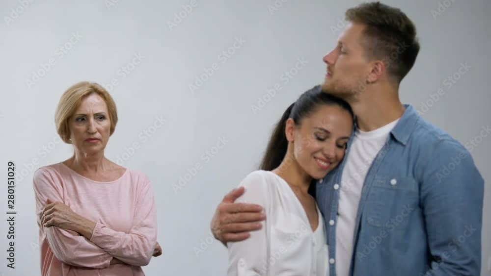 Offended mother-in-law looking at couple tenderly hugging, lack of attention Offended mother-in-law looking at couple tenderly hugging, lack of attention