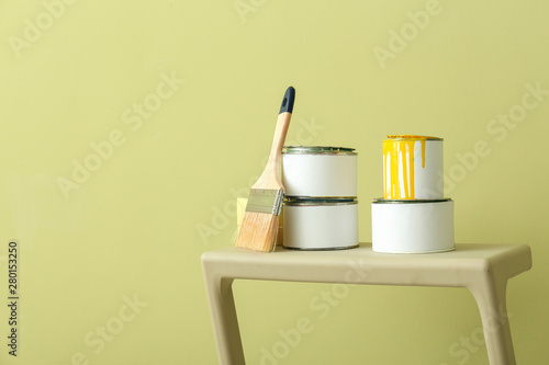 Cans of paint with brush on step ladder against color background photo