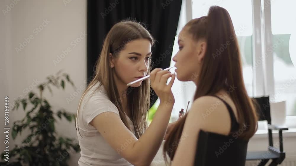 Beautiful makeup artist applies lipstick. Hand of make-up master, painting lips of young beauty redhead model. Make up in process