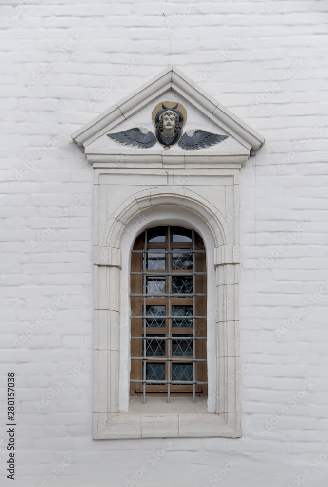 Old arched window with metall lattice and relief on a white brick wall of christian church Old arched window with metall lattice and relief on a white brick wall of christian church