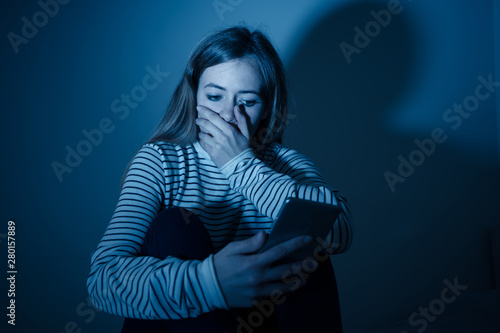 Depressed teenager girl on mobile phone victim of cyberbullying feeling sad, unhappy and lonely