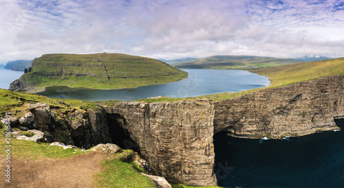 Most beautiful landmark of Vagar island - Leitisvatn lake. Amazing panorama with lake above the ocean and cliffs. Faroe Islands.