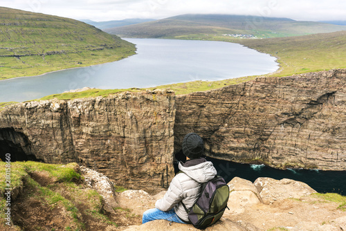 Traveller is sitting on cliff upfront of Sorvagsvatn lake. Vagar, Faroe Islands.