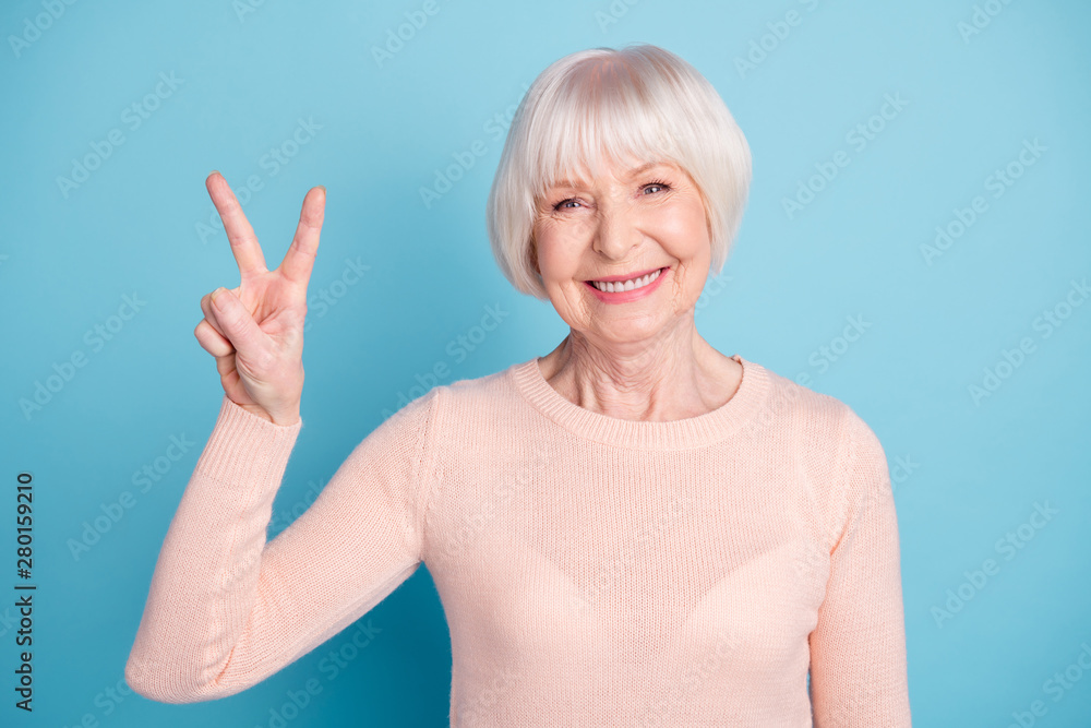 Portrait of cute person making v-sign looking with beaming smile wearing pastel sweater isolated over blue background Portrait of cute person making v-sign looking with beaming smile wearing pastel sweater isolated over blue background
