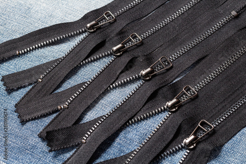 Pack a lot of black metal brass zippers stripes with sliders pattern for handmade sewing tailoring leatherwork leathercraft on the blue wooden background