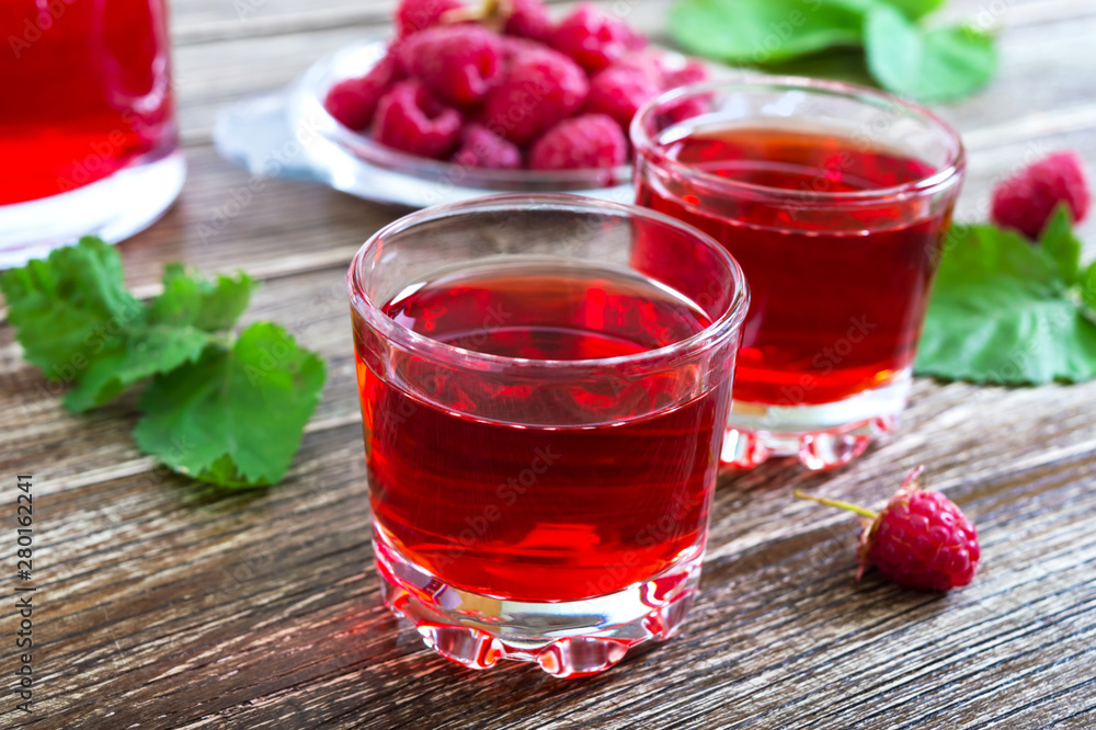 Raspberry liqueur in glass, fresh natural ripe organic berries and green leaves on a rustic wood background. Alcoholic flavored drink. Raspberry liqueur in glass, fresh natural ripe organic berries and green leaves on a rustic wood background. Alcoholic flavored drink.