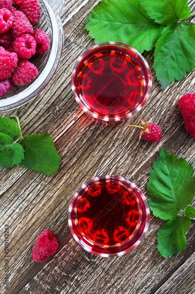 Raspberry liqueur in glass, fresh natural ripe organic berries and green leaves on a rustic wood background. Alcoholic flavored drink. Raspberry liqueur in glass, fresh natural ripe organic berries and green leaves on a rustic wood background. Alcoholic flavored drink.