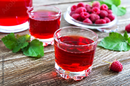 Raspberry liqueur in glass, fresh natural ripe organic berries and green leaves on a rustic wood background. Alcoholic flavored drink.