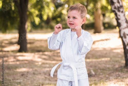 One little boy in white kimono during training karate kata exercises in summer outdoors