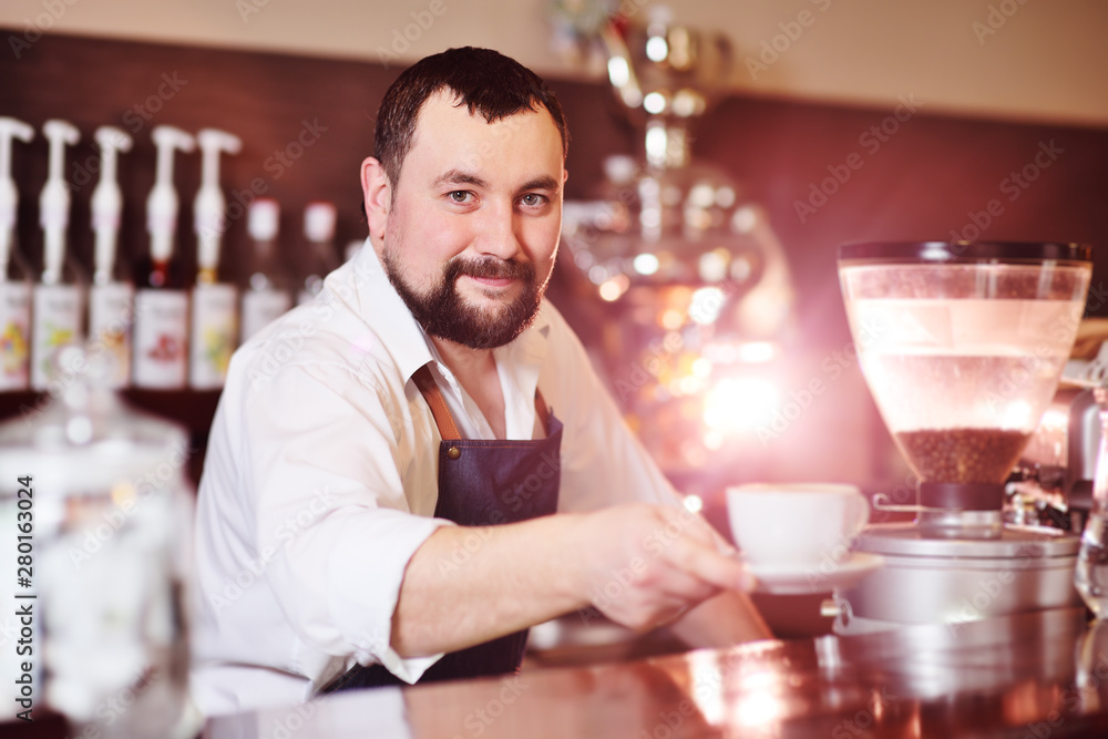 portrait of a handsome bearded barista preparing coffee on the background of a coffee shop and a coffee machine
