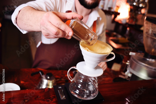 barista or coffee barman prepares coffee by an alternative method of brewing - pour over - by hot water spilling through a special filter with ground powder