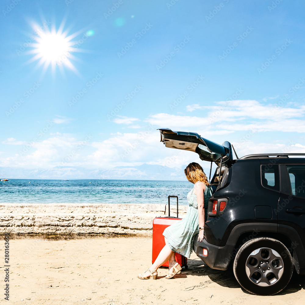 A woman in a black car on a sandy beach and blue ocean view.