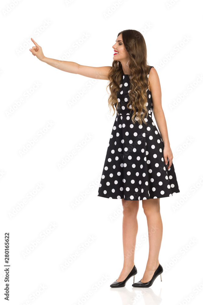 Beautiful Young Woman In Black Cocktail Dress In Polka Dots And High Heels Is Touching Something Beautiful Young Woman In Black Cocktail Dress In Polka Dots And High Heels Is Touching Something