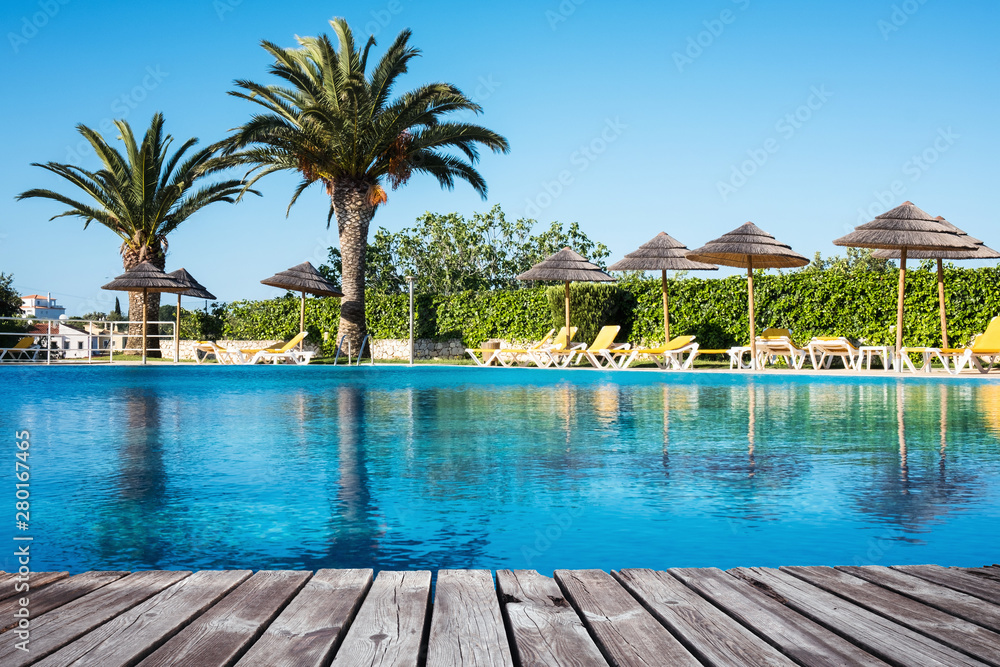 Image of wooden table in front with blurred background of swimming pool in beautiful beach resort, Thailand.