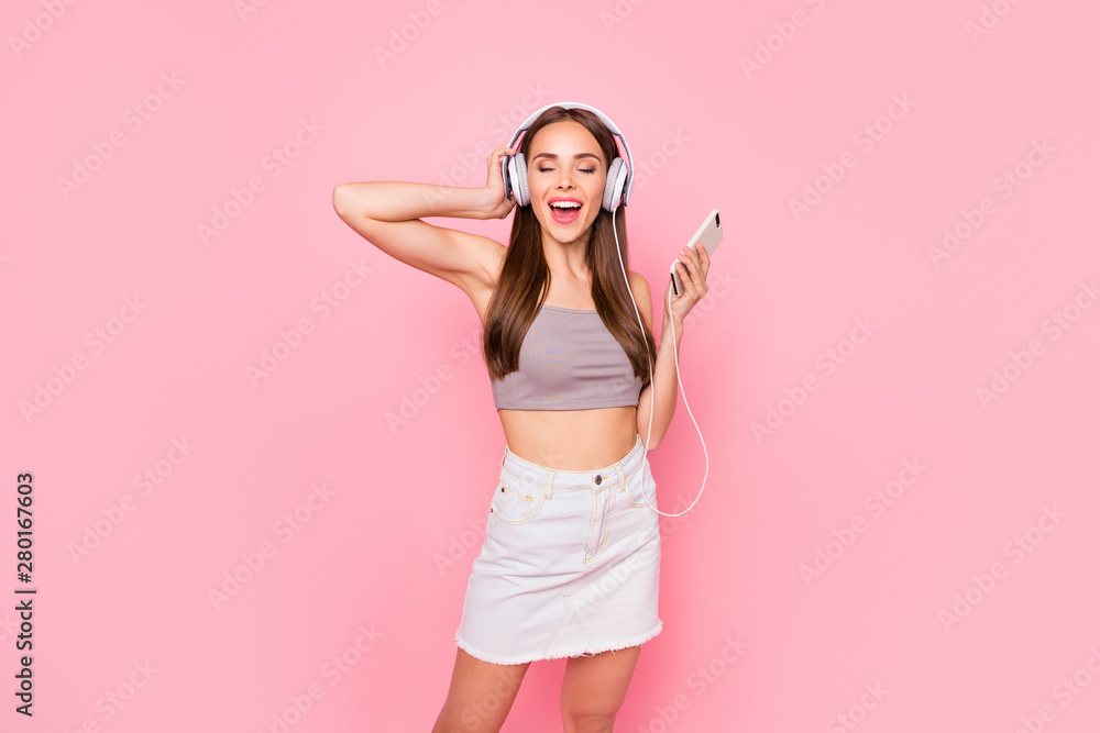 Portrait of lovely youth with her eyes closed holding modern technology wearing white skirt denim jeans grey tank-top isolated over pink background Portrait of lovely youth with her eyes closed holding modern technology wearing white skirt denim jeans grey tank-top isolated over pink background