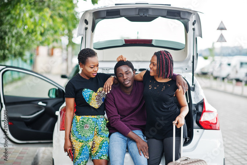 Three african american friends sit in the trunk of the car.