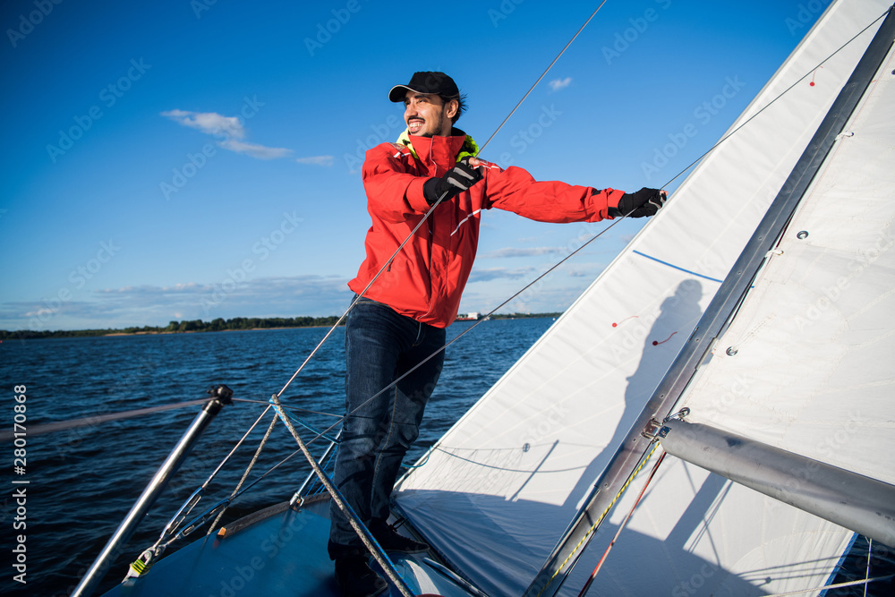 Low angle view of sailor operating windlass on yacht. Working with ropes and sail Low angle view of sailor operating windlass on yacht. Working with ropes and sail