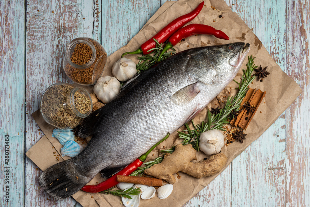 Fresh Raw Sea Bass on wooden table surrounded by fresh ingredients and spices. Fresh Raw Sea Bass on wooden table surrounded by fresh ingredients and spices.