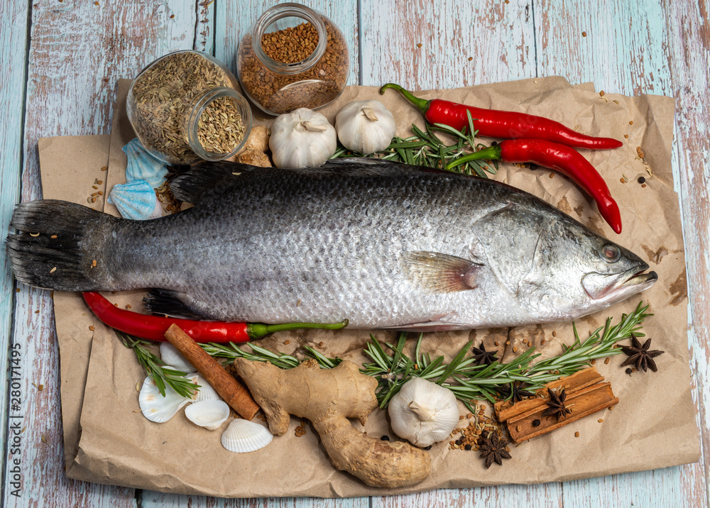 Fresh Raw Sea Bass on wooden table surrounded by fresh ingredients and spices. Fresh Raw Sea Bass on wooden table surrounded by fresh ingredients and spices.