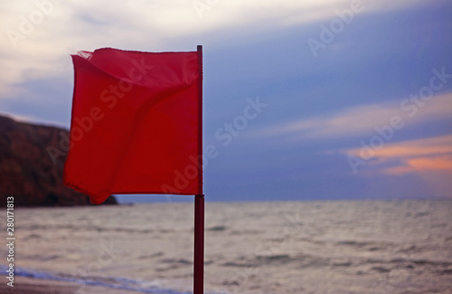 Red flag on the beach, sea and stormy sky in background