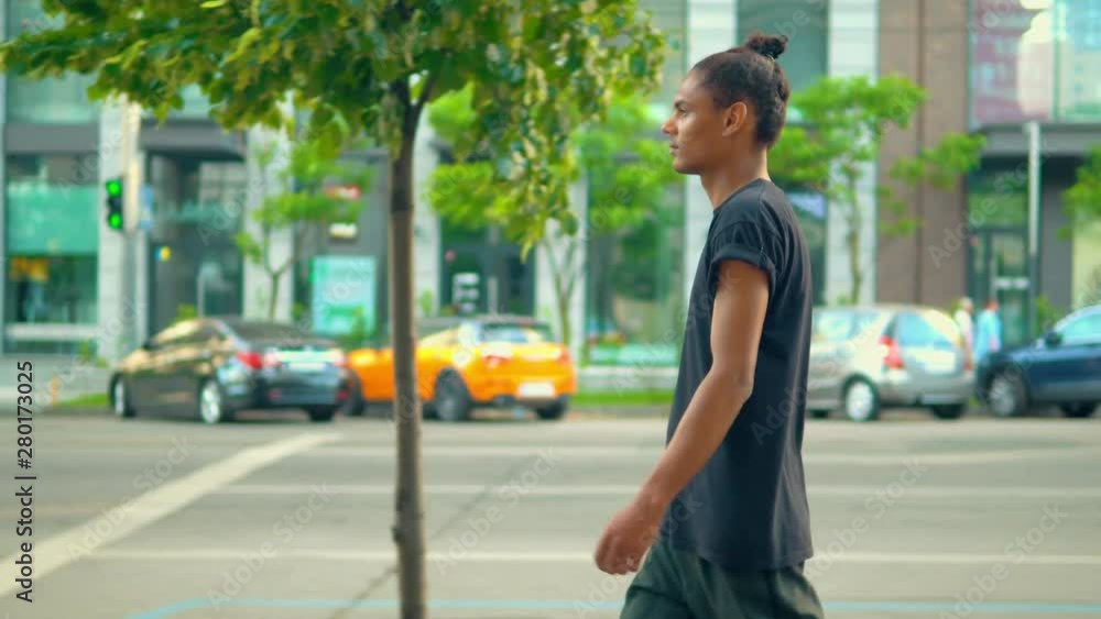 side view young man walking in the modern city along the road with parked cars near the building side view young man walking in the modern city along the road with parked cars near the building