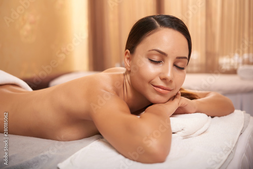 Young beautiful woman lying on massage table with eyes closed and resting after massage in beauty salon