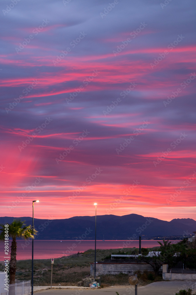 Scenic red sunrise over coastline with sandy beach and clear sea water in Alcamo Marina, small town in Sicily, Italy, summer vacation destination