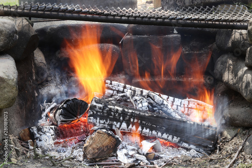 Burning logs flaming in a barbecue fire. Homemade camp fire with black gridiron. Outdoor lifestyle and natural fuel.